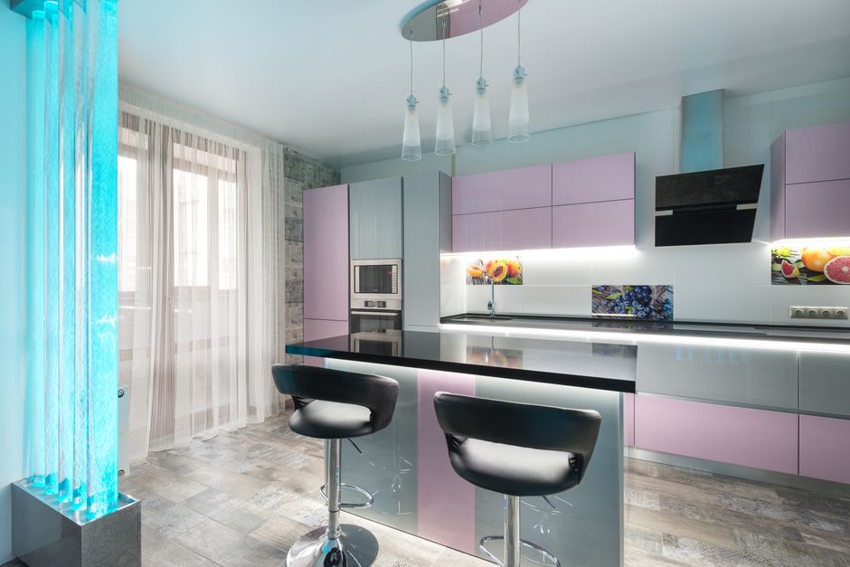 A modern kitchen with a sleek grey base and upper cabinets, featuring a black countertop and a stainless steel extractor hood mounted above. The kitchen has a wood-paneled backsplash with open shelvin